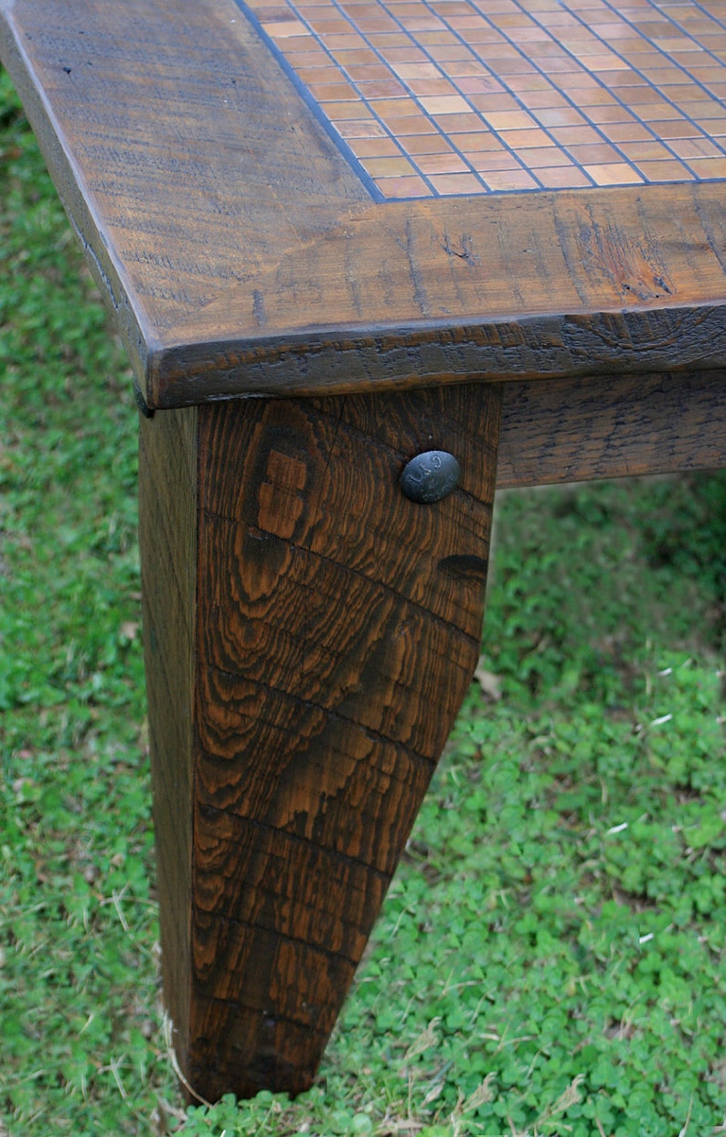 May include: A close-up of a wooden table leg with a dark brown stain. The leg is made of reclaimed wood and has a rustic look. A metal nail is visible on the leg.