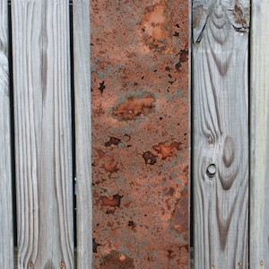 May include: A rectangular piece of metal with a rusty, orange, and blue patina. The metal is mounted on a wooden fence.