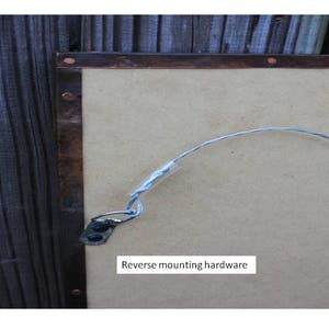 May include: A close-up of the back of a copper framed mirror with a wire hanging system. The text "Reverse mounting hardware" is visible on the mirror.