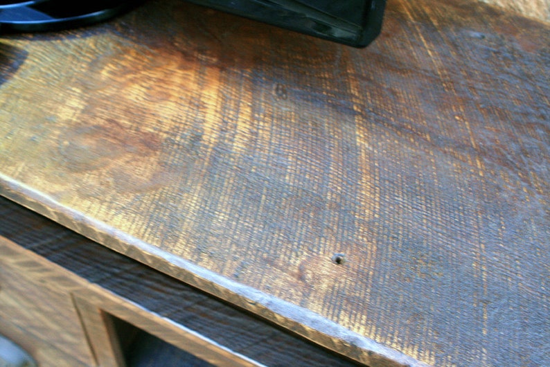 May include: Close-up of a dark brown wooden surface with a light brown stain. The surface has a rough, textured grain and a slight sheen.