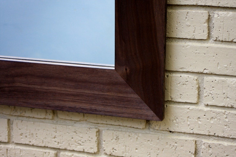 May include: A close-up of a dark brown wooden frame with a light blue background. The frame is mounted on a white brick wall.