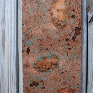May include: A close-up of a copper sheet with a blue-green patina. The copper has a rustic, weathered look with areas of oxidation and discoloration.