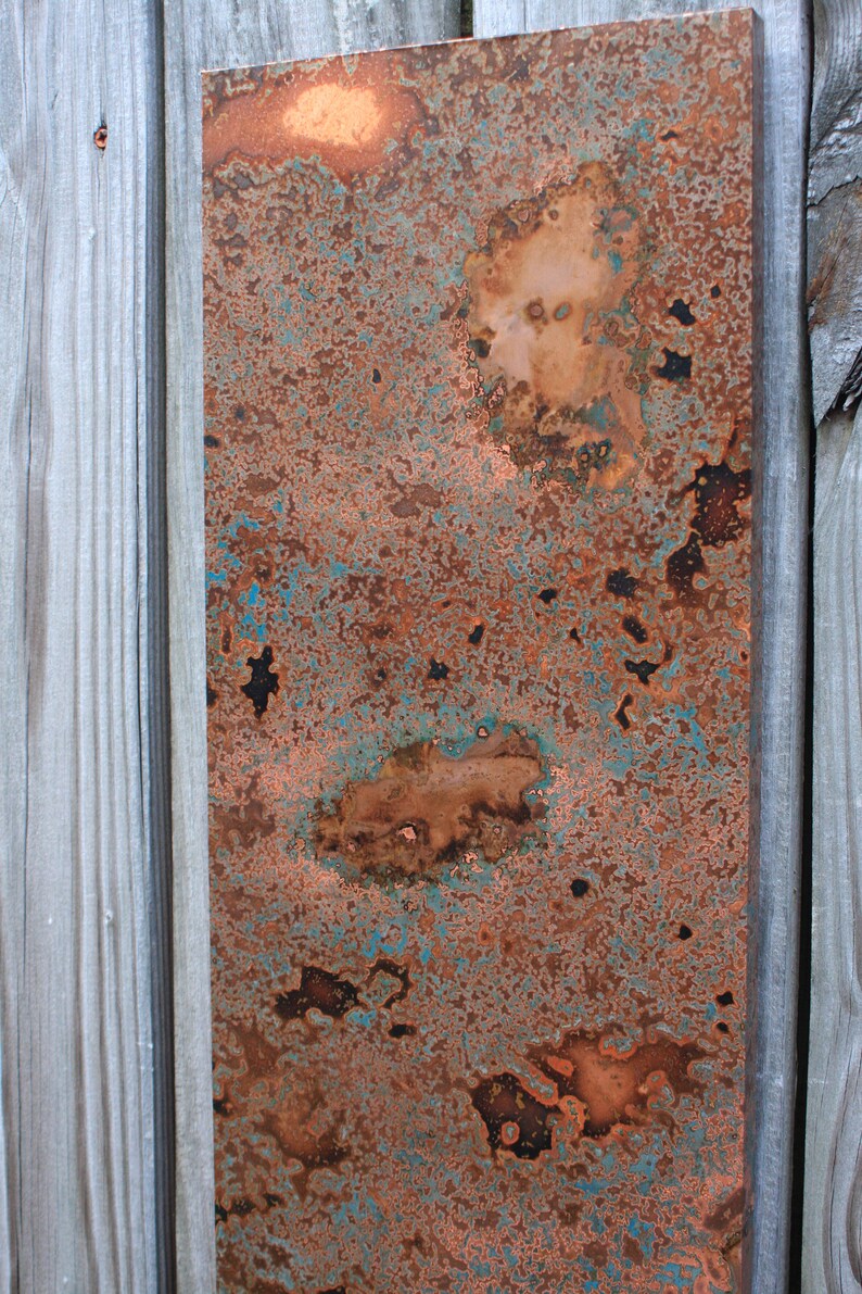 May include: A close-up of a copper sheet with a blue-green patina. The copper has a rustic, weathered look with areas of oxidation and discoloration.