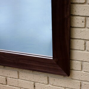 May include: A dark brown wooden frame surrounds a large mirror, mounted on a light beige brick wall.