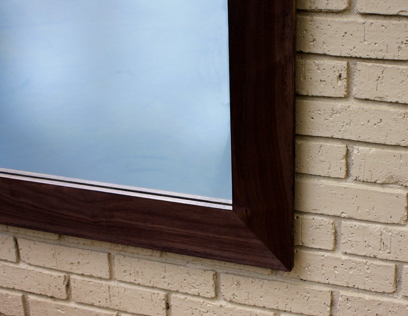 May include: A dark brown wooden frame surrounds a large mirror, mounted on a light beige brick wall.