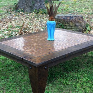 May include: A rustic wooden coffee table with a mosaic tile top. The table has a dark brown stain and features a decorative metal accent on each leg. A blue vase with feathers sits on the table.