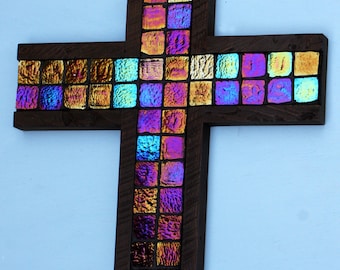 May include: A wooden cross with a mosaic of iridescent glass tiles in shades of purple, blue, and gold. The cross is a religious symbol and a decorative piece for the home.