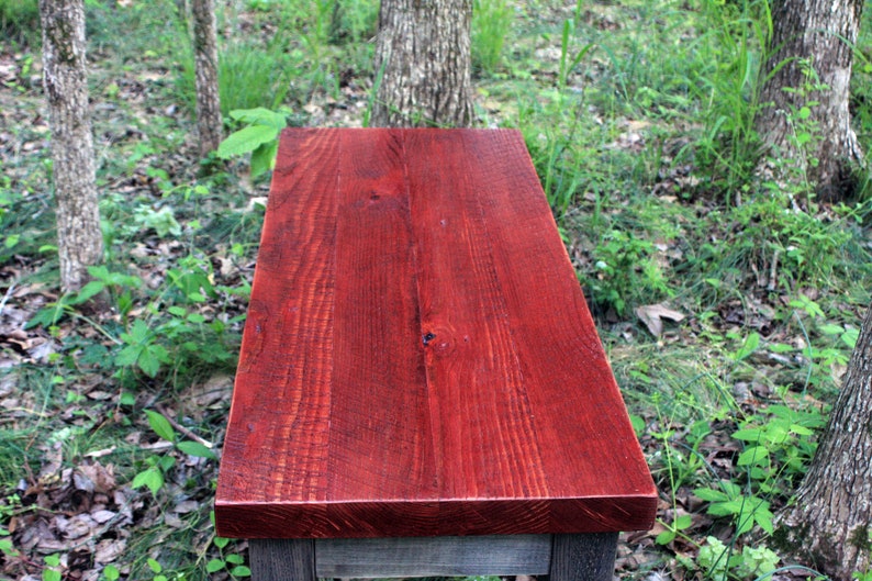 May include: A rustic wooden table top with a rich red stain. The table top is made of reclaimed wood and has a natural, distressed look.