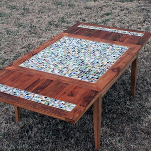 May include: A wooden table with a mosaic tile top. The tiles are made of small, colorful pieces of glass. The table has a rustic, handmade look.