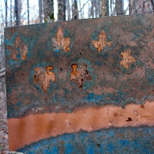 May include: A metal sheet with a blue and brown patina. The sheet has a horizontal line of copper running across the middle. There are several leaf shapes pressed into the metal.