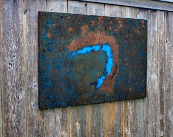 Könnte beinhalten: Rechteckiges Metallkunstwerk mit einer strukturierten, verwitterten Oberfläche. Das Kunstwerk zeigt eine Mischung aus Braun-, Türkis- und Blautönen, mit einer hellblauen, gebogenen Form in der Mitte. Auf einer verwitterten Holzwand montiert.