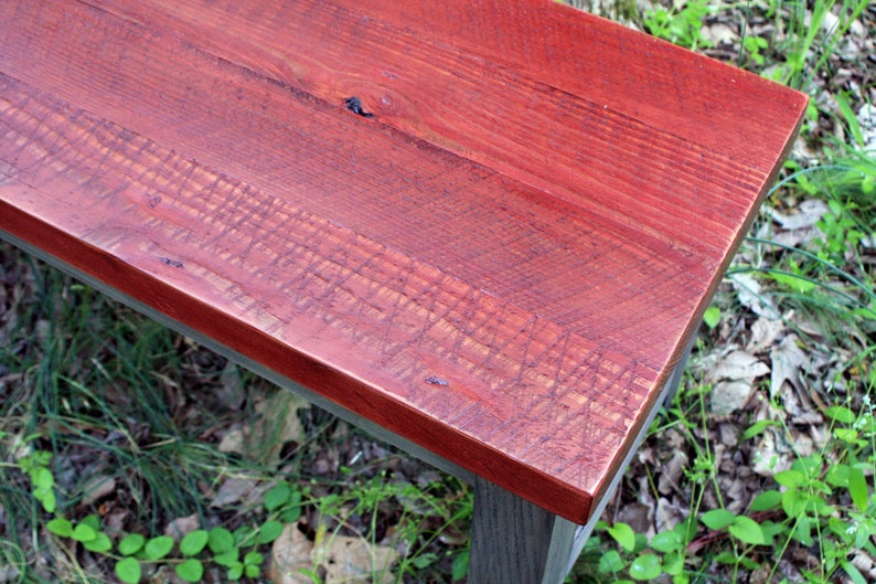 May include: A close-up of a wooden bench with a red stained top. The bench has a dark gray base and is made of reclaimed wood.