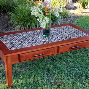 May include: A wooden coffee table with a mosaic tile top and three drawers. The table is a rich mahogany color and has a simple, elegant design.