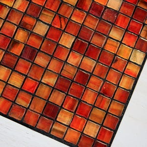 K&ouml;nnte beinhalten: Nahaufnahme eines roten, orangefarbenen und braunen Mosaikmusters. Die Fliesen sind in einem Gittermuster angeordnet und durch schwarzen Fugenm&ouml;rtel getrennt.