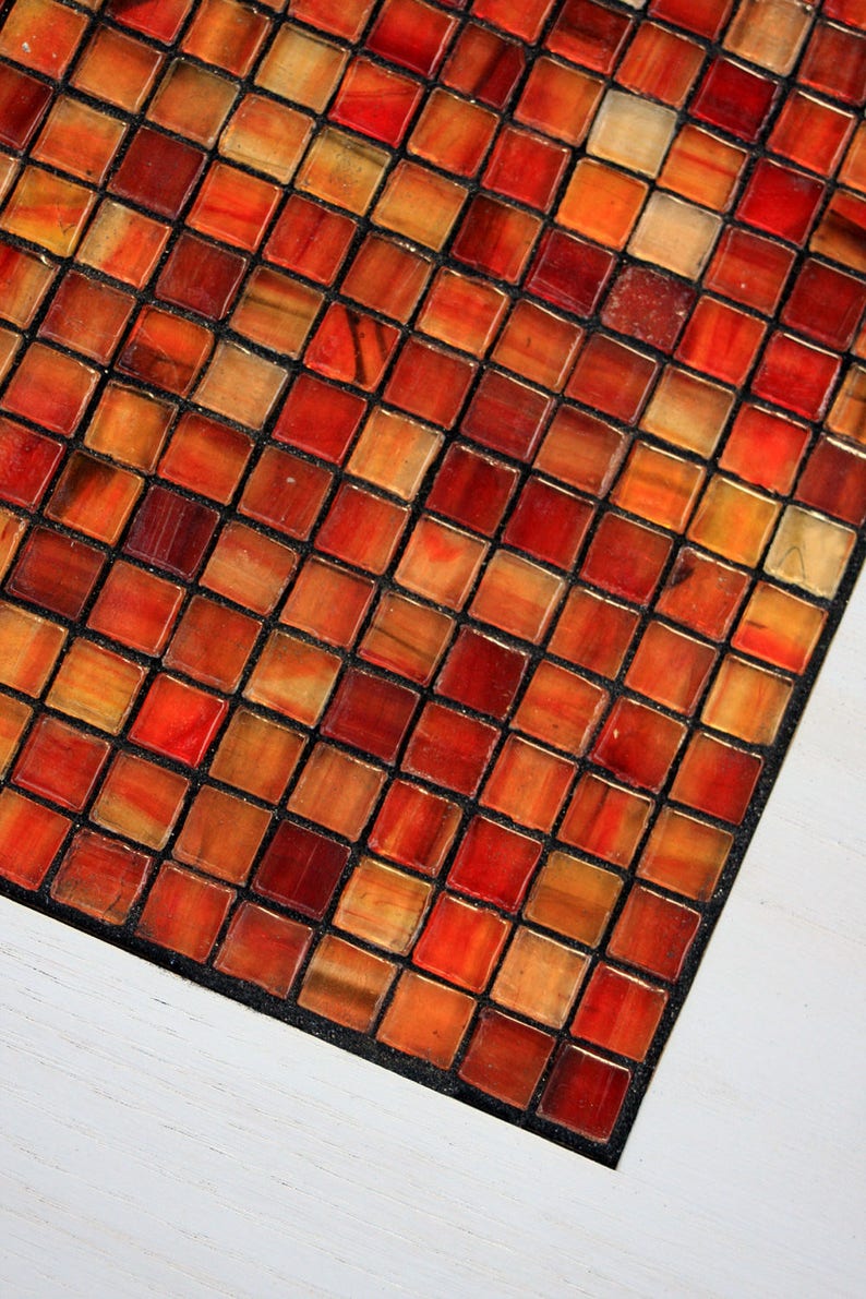 K&ouml;nnte beinhalten: Nahaufnahme eines roten, orangefarbenen und braunen Mosaikmusters. Die Fliesen sind in einem Gittermuster angeordnet und durch schwarzen Fugenm&ouml;rtel getrennt.