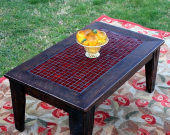 May include: A dark wood coffee table with a red tile top. The table is sitting on a rug with a floral pattern.