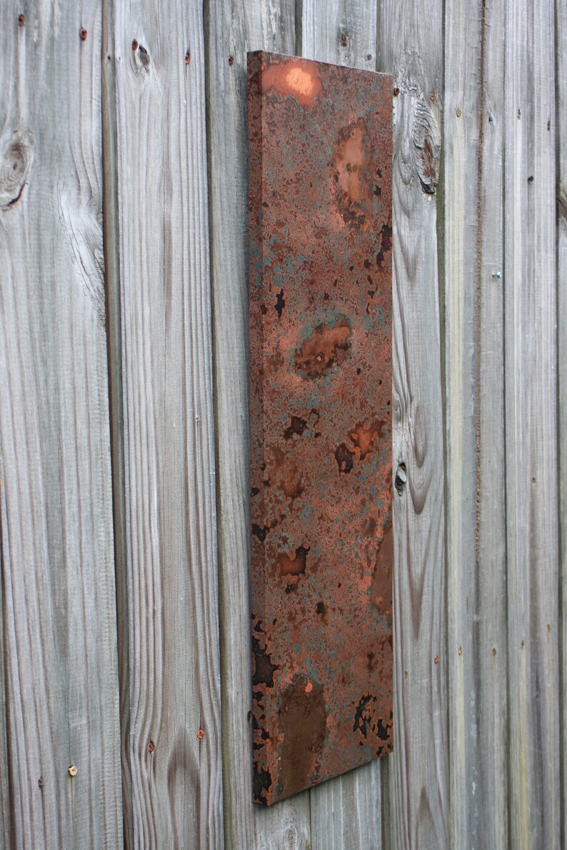 May include: A rectangular copper panel with a rustic, weathered finish. The panel has a mottled appearance with shades of orange, brown, and green. The panel is mounted on a wooden wall.