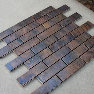 May include: A sheet of copper tile with a brushed finish. The tiles are arranged in a herringbone pattern.