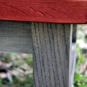 May include: A wooden table with a red stained top and gray stained legs. The table is made of wood with a visible grain pattern.
