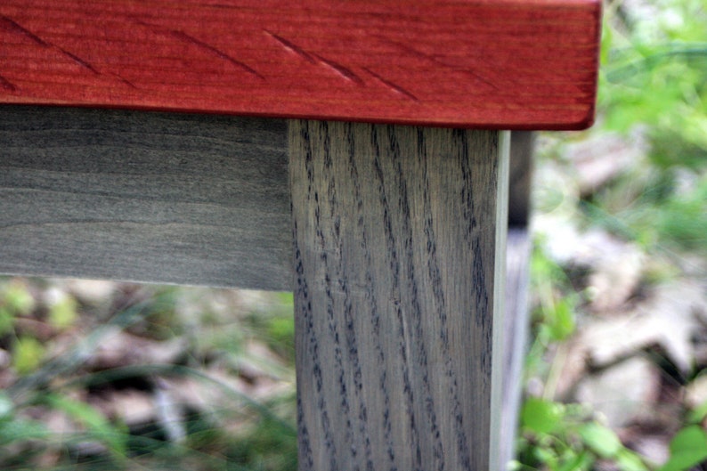 May include: A wooden table with a red stained top and gray stained legs. The table is made of wood with a visible grain pattern.