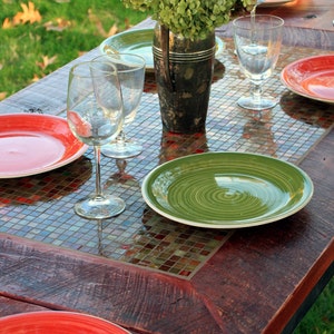 K&ouml;nnte beinhalten: Ein rustikaler Holztisch mit einer Mosaik-Tischplatte. Der Tisch ist mit roten und gr&uuml;nen Tellern, Weingl&auml;sern und einer Vase mit gr&uuml;nen Blumen gedeckt.