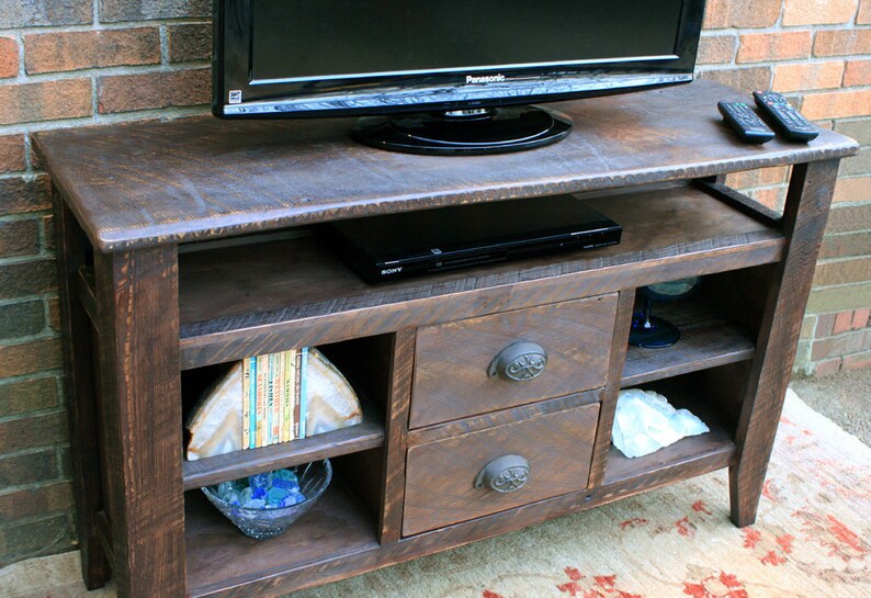 May include: A dark brown wooden TV stand with two drawers and open shelves. The stand has a distressed finish and features decorative metal drawer pulls. A flat screen TV and a DVD player are on top of the stand.