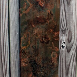 May include: A rectangular metal panel with a mottled, rusty, and green patina. The panel is mounted on a wooden wall.