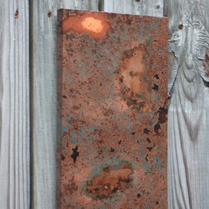 May include: A close-up of a rusty metal sheet with a copper patina. The metal has a mottled appearance with shades of brown, orange, and green.