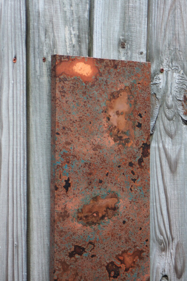 May include: A close-up of a rusty metal sheet with a copper patina. The metal has a mottled appearance with shades of brown, orange, and green.