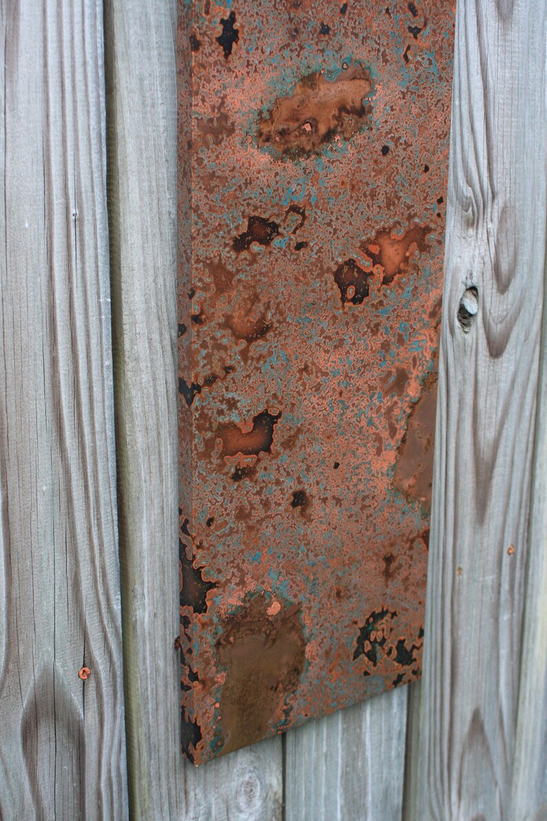 May include: A close-up of a rectangular piece of copper metal with a patina finish. The copper has a mottled appearance with shades of brown, orange, and green.