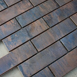 May include: A close-up of a copper metal tile sheet with a brushed finish. The tiles are arranged in a brick pattern and have a dark brown and blue colour.