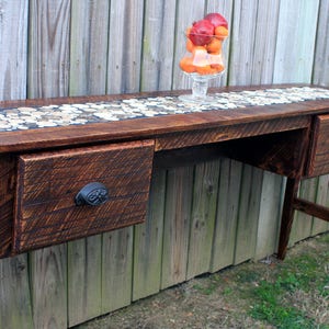 May include: A rustic wooden console table with two drawers and a mosaic tile top. The table has a dark brown stain and is accented with black metal drawer pulls.