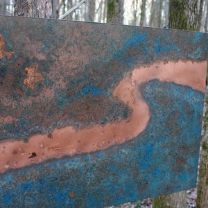May include: A copper metal wall art piece with a blue and brown patina. The piece features a long, thin, winding line of copper that resembles a river.