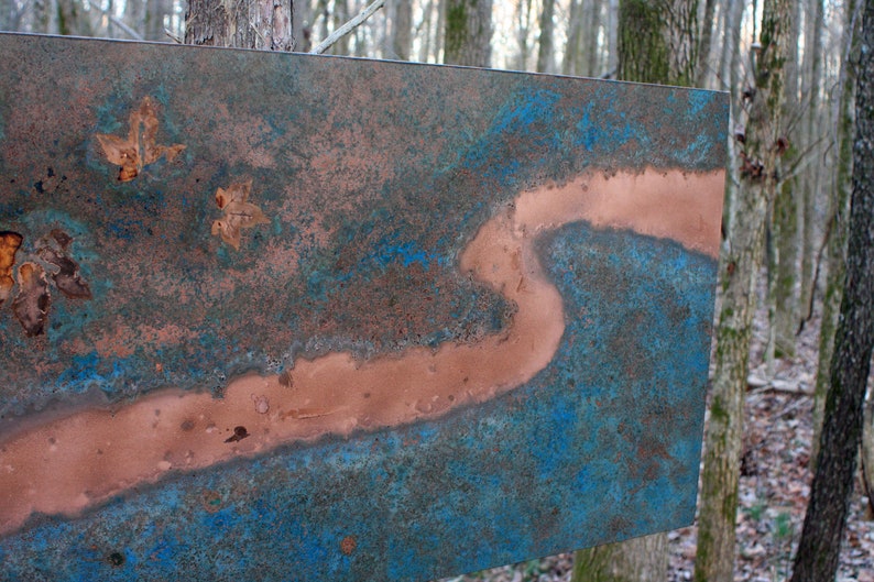 May include: A copper metal wall art piece with a blue and brown patina. The piece features a long, thin, winding line of copper that resembles a river.