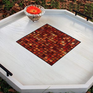 K&ouml;nnte beinhalten: Wei&szlig;es achteckiges Serviertablett mit schwarzen Griffen und einem roten und orangefarbenen Mosaik-Fliesendesign in der Mitte.