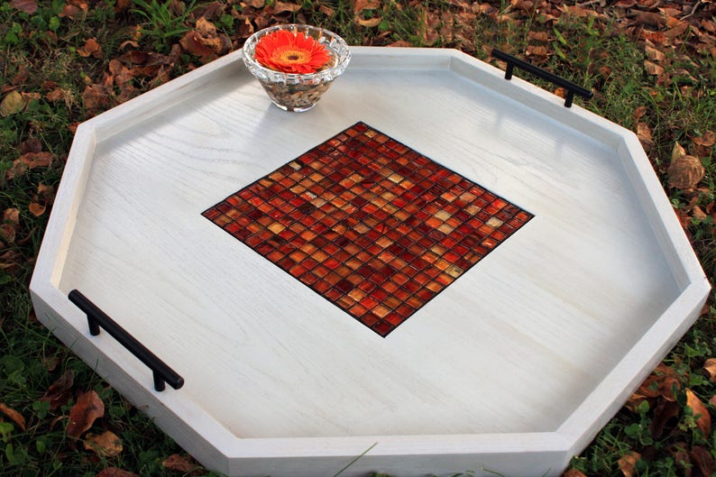 K&ouml;nnte beinhalten: Wei&szlig;es achteckiges Serviertablett mit schwarzen Griffen und einem roten und orangefarbenen Mosaik-Fliesendesign in der Mitte.