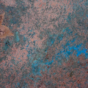 May include: A close-up of a textured surface with a blue and pink color scheme. A single, dried leaf is lying on the surface.