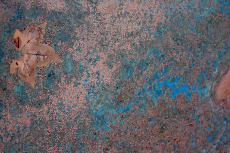 May include: A close-up of a textured surface with a blue and pink color scheme. A single, dried leaf is lying on the surface.