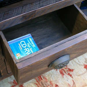 May include: A wooden entertainment center with a drawer that is open, revealing a blue and white CD-RW disc inside. The drawer has a metal handle.