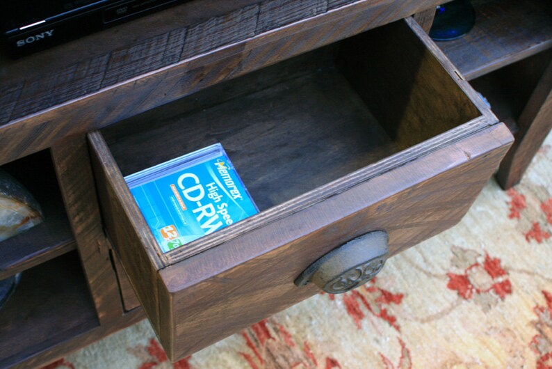 May include: A wooden entertainment center with a drawer that is open, revealing a blue and white CD-RW disc inside. The drawer has a metal handle.