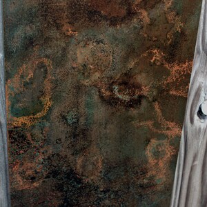 May include: A close-up of a weathered wooden surface with a rusty metal panel behind it. The wood has a natural grain pattern and is painted a light gray color. The metal panel has a mottled brown and green patina with hints of orange.