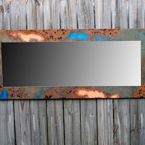 May include: A rectangular mirror with a rustic, metallic frame. The frame has a distressed look with shades of copper, blue, and brown.
