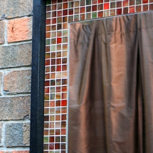 May include: A black framed window with a brown curtain and a mosaic of small red, brown, and white tiles.