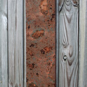 May include: A rectangular metal panel with a rusty, mottled surface. The panel is a mix of orange, brown, and green hues, with a distressed, aged look.