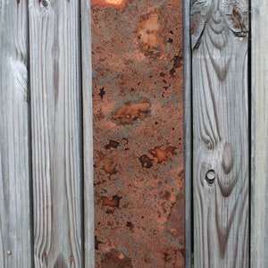 May include: A rectangular piece of copper metal with a rusty patina. The metal is attached to a wooden wall.