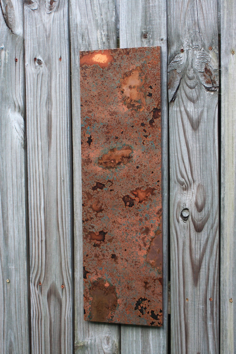 May include: A rectangular piece of copper metal with a rusty patina. The metal is attached to a wooden wall.