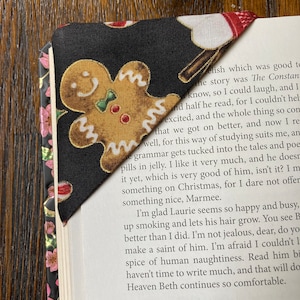 May include: A black fabric bookmark with a gingerbread man design. The bookmark is folded over the corner of a book with text that reads "A Happy New Year to you all, my dear course includes Mr. L. and a young man b I can't tell you how much I enjoyed your C"