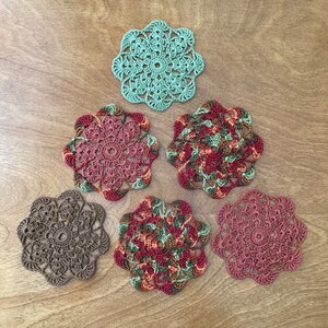May include: Six crocheted doilies in various colors, including green, brown, and red. The doilies are arranged in a circular pattern on a wooden surface.