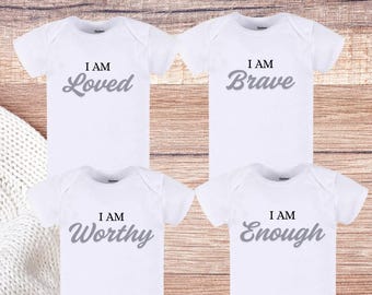 May include: Four white newborn onesies with affirmation designs. Each onesie has a different affirmation in gray text: "I AM Loved", "I AM Brave", "I AM Worthy", and "I AM Enough". The text "Personalized Newborn Onesies 4-Pack Affirmation Designs" is at the top.