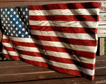 Op de afbeelding: Een Amerikaanse vlag van hout, geschilderd in rood, wit en blauw. De vlag is gegraveerd om eruit te zien alsof hij in de wind waait.